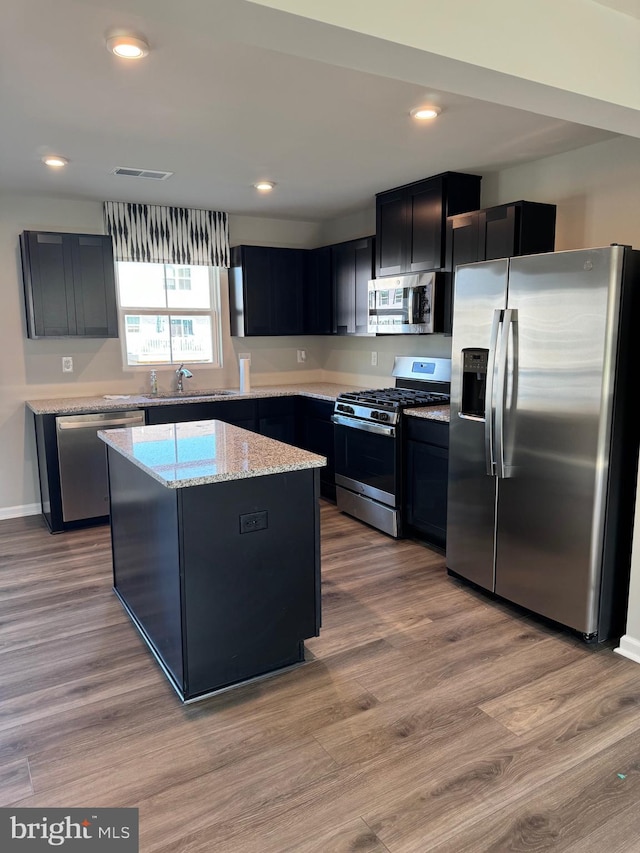 kitchen with sink, light stone countertops, light hardwood / wood-style floors, a kitchen island, and stainless steel appliances