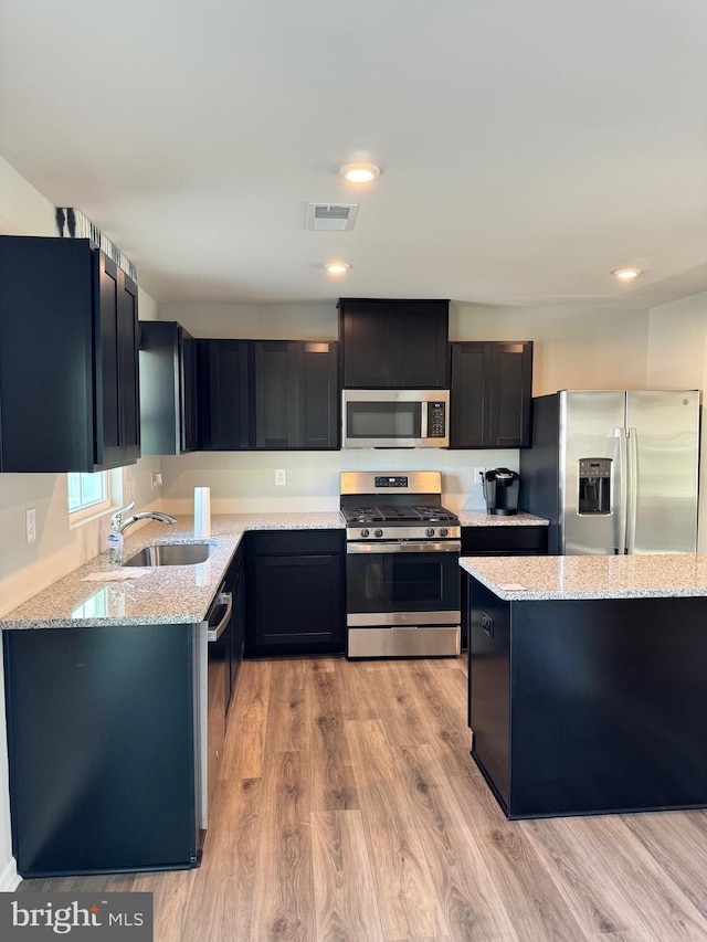 kitchen with light hardwood / wood-style floors, light stone countertops, sink, and appliances with stainless steel finishes