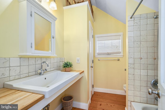 bathroom with toilet, decorative backsplash, tiled shower / bath combo, lofted ceiling, and hardwood / wood-style flooring