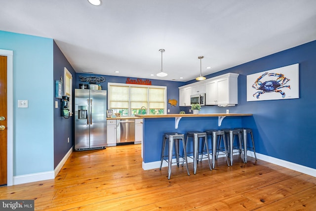 kitchen featuring stainless steel appliances, kitchen peninsula, hanging light fixtures, white cabinetry, and a kitchen breakfast bar