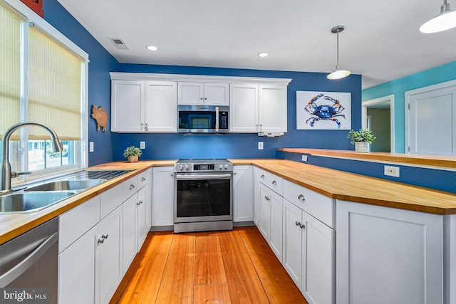 kitchen with white cabinets, hanging light fixtures, sink, appliances with stainless steel finishes, and butcher block counters