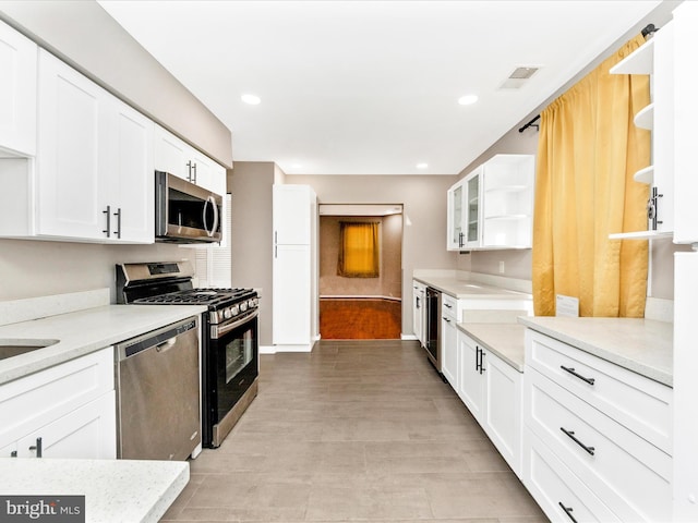 kitchen with light stone countertops, white cabinetry, beverage cooler, stainless steel appliances, and light wood-type flooring