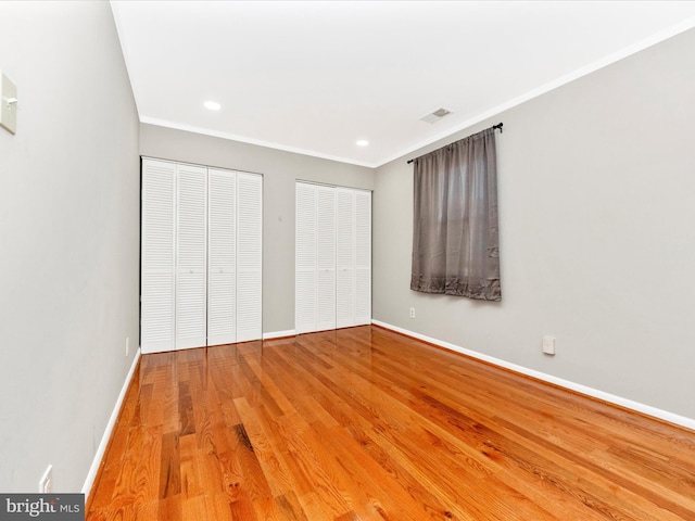 unfurnished bedroom with light hardwood / wood-style floors, crown molding, and two closets