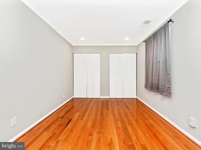 unfurnished bedroom featuring wood-type flooring, ornamental molding, and two closets