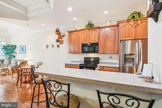 kitchen featuring kitchen peninsula, light wood-type flooring, a breakfast bar area, black appliances, and ornamental molding