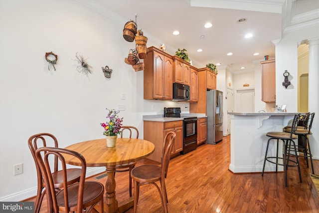 kitchen with a kitchen breakfast bar, decorative columns, crown molding, black appliances, and hardwood / wood-style flooring