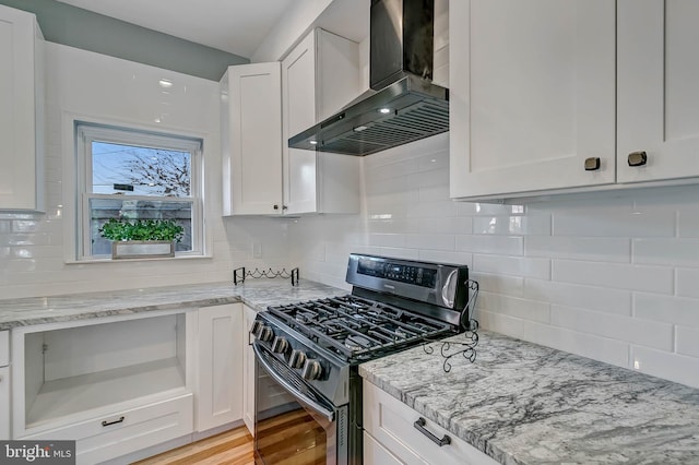 kitchen featuring white cabinets, wall chimney range hood, light stone countertops, light wood-type flooring, and stainless steel range with gas stovetop