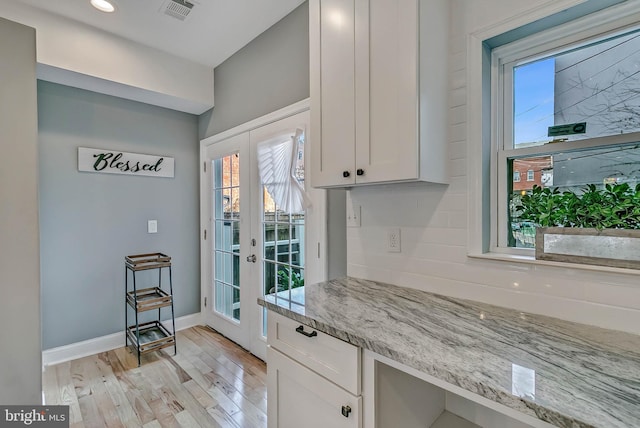 kitchen featuring light stone counters, french doors, white cabinets, and light hardwood / wood-style flooring