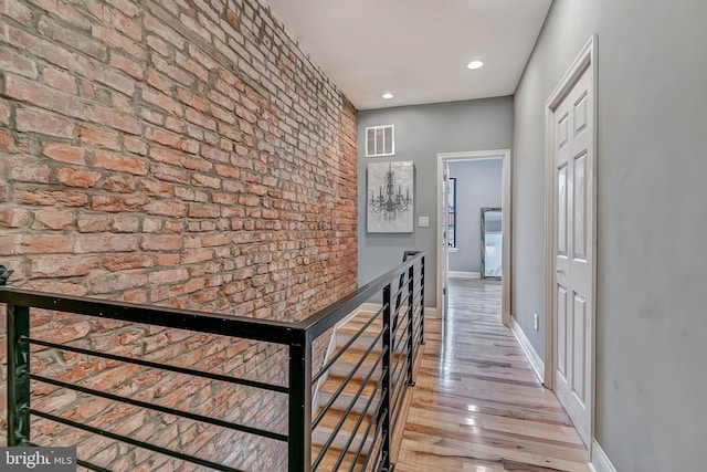 hallway featuring brick wall and light hardwood / wood-style floors