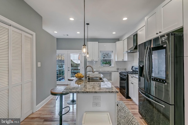 kitchen featuring black range with gas stovetop, sink, hanging light fixtures, wall chimney exhaust hood, and stainless steel fridge