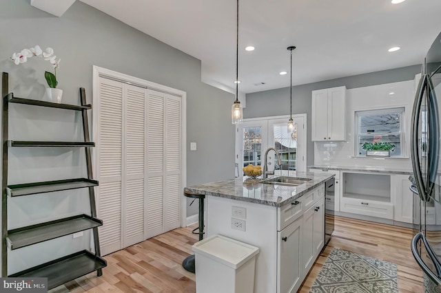 kitchen with light stone countertops, a kitchen island with sink, sink, light hardwood / wood-style flooring, and white cabinets