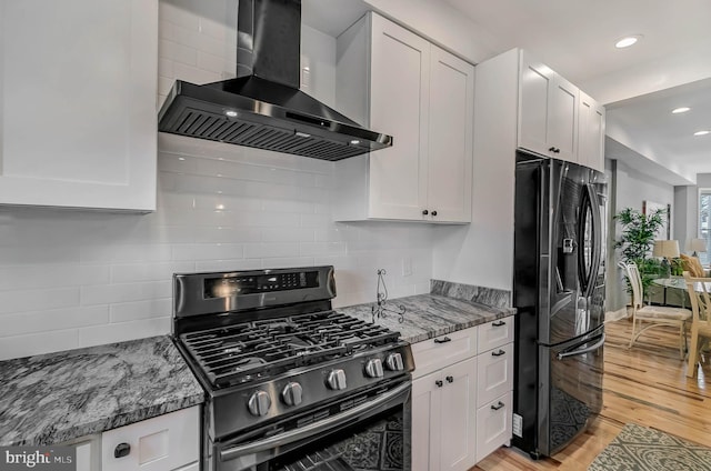 kitchen featuring fridge with ice dispenser, white cabinetry, wall chimney range hood, stainless steel range with gas cooktop, and light wood-type flooring