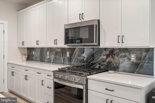 kitchen with white cabinets, backsplash, appliances with stainless steel finishes, and light wood-type flooring