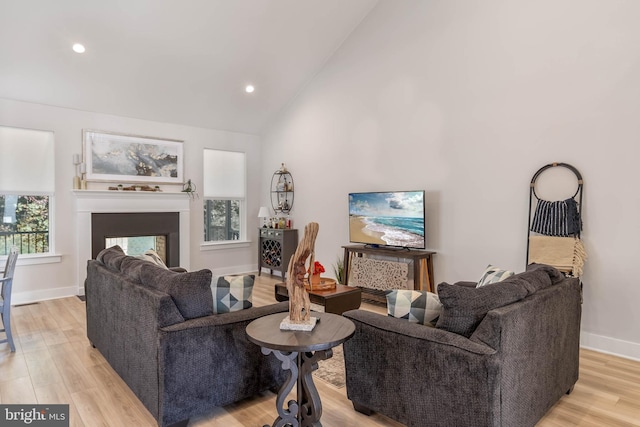 living room featuring a multi sided fireplace, light hardwood / wood-style flooring, and high vaulted ceiling