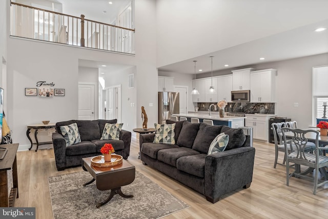 living room with sink, a towering ceiling, and light hardwood / wood-style floors