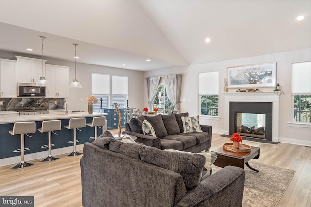 living room featuring sink, a multi sided fireplace, light hardwood / wood-style flooring, and high vaulted ceiling