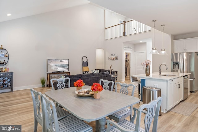 dining space with sink, light hardwood / wood-style flooring, and a towering ceiling