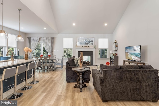 living room featuring sink, a multi sided fireplace, light hardwood / wood-style flooring, and high vaulted ceiling