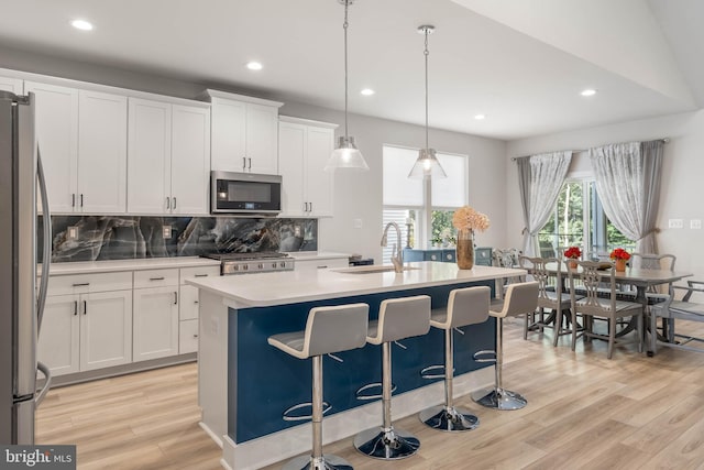 kitchen featuring white cabinets, a kitchen island with sink, hanging light fixtures, and appliances with stainless steel finishes