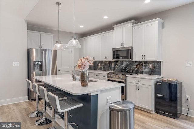 kitchen featuring white cabinets, decorative light fixtures, stainless steel appliances, backsplash, and a center island with sink