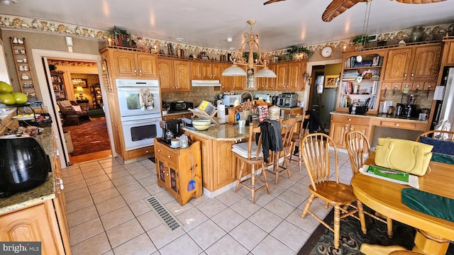 kitchen with light tile patterned floors, white double oven, pendant lighting, and light stone counters