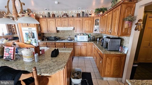 kitchen with decorative backsplash, a kitchen bar, light tile patterned flooring, light stone counters, and white appliances