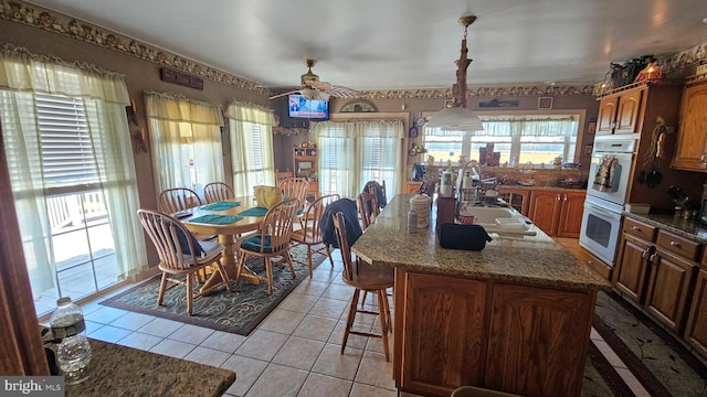 kitchen with double oven, a kitchen island with sink, sink, decorative light fixtures, and ceiling fan