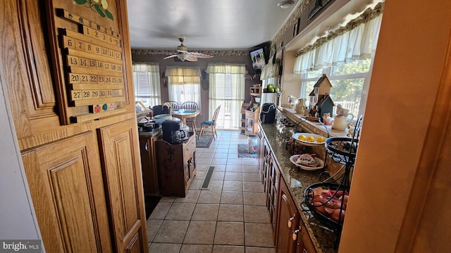 interior space featuring a wealth of natural light, tile patterned floors, dark stone countertops, and ceiling fan