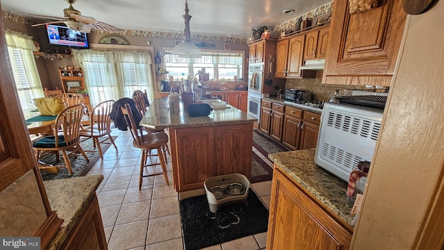 kitchen with light stone counters, a wealth of natural light, decorative light fixtures, and a kitchen island