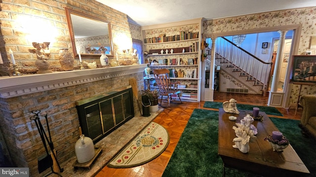 living room featuring a textured ceiling, ornate columns, a fireplace, and parquet floors