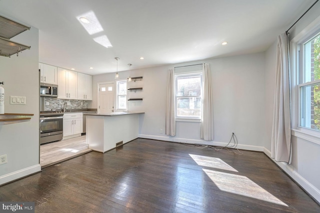 kitchen featuring white cabinets, kitchen peninsula, decorative light fixtures, stainless steel appliances, and dark hardwood / wood-style floors