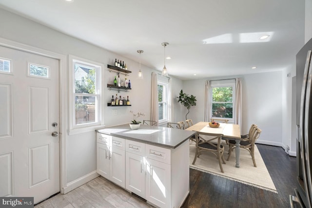 kitchen featuring stainless steel refrigerator, hanging light fixtures, white cabinets, and hardwood / wood-style floors