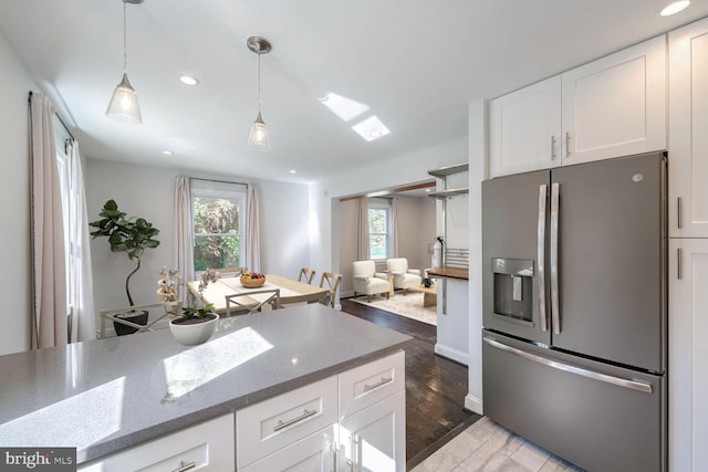 kitchen featuring wood-type flooring, stainless steel fridge, light stone counters, and white cabinetry