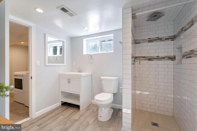 bathroom with wood-type flooring, tiled shower, vanity, and toilet