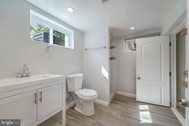 bathroom with tiled shower, hardwood / wood-style flooring, vanity, and toilet