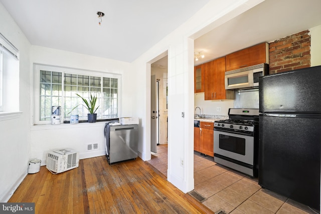 kitchen featuring appliances with stainless steel finishes, brown cabinetry, light countertops, hardwood / wood-style floors, and baseboards