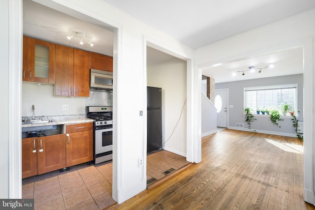 kitchen featuring stainless steel gas range oven, a sink, freestanding refrigerator, and brown cabinets