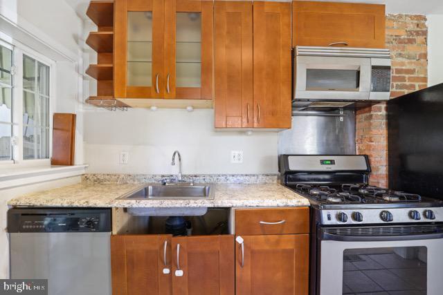 kitchen with appliances with stainless steel finishes, a sink, glass insert cabinets, and light stone countertops