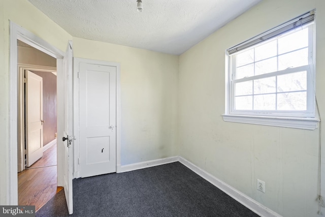 empty room with a textured ceiling, baseboards, and dark carpet