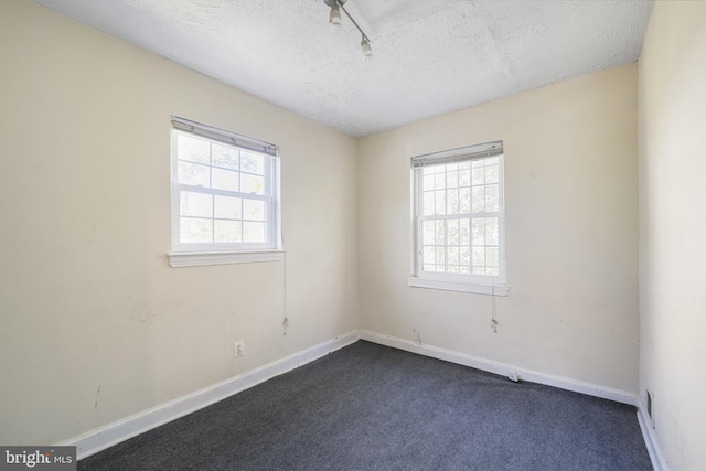 empty room with plenty of natural light, a textured ceiling, dark colored carpet, and baseboards