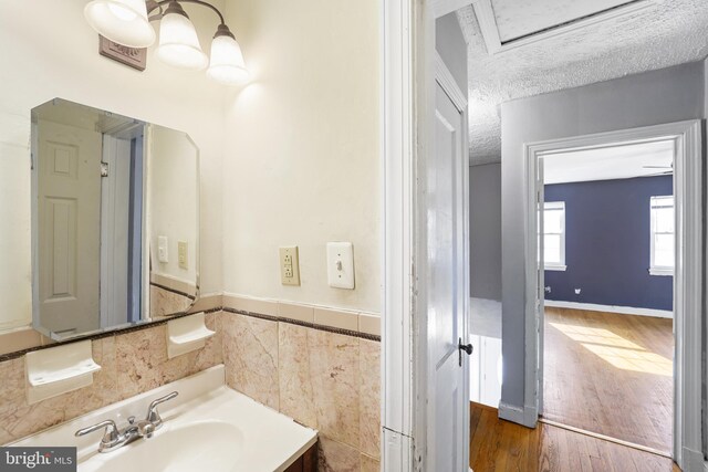 bathroom with wood finished floors, a textured ceiling, tile walls, vanity, and a wainscoted wall