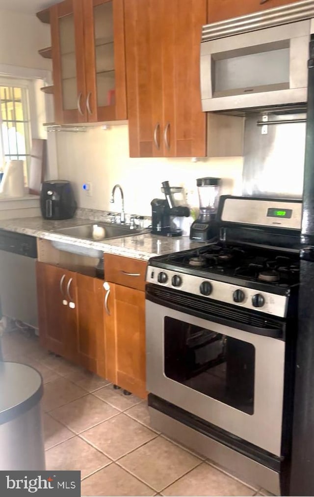 kitchen featuring light stone counters, sink, light tile patterned floors, and stainless steel appliances