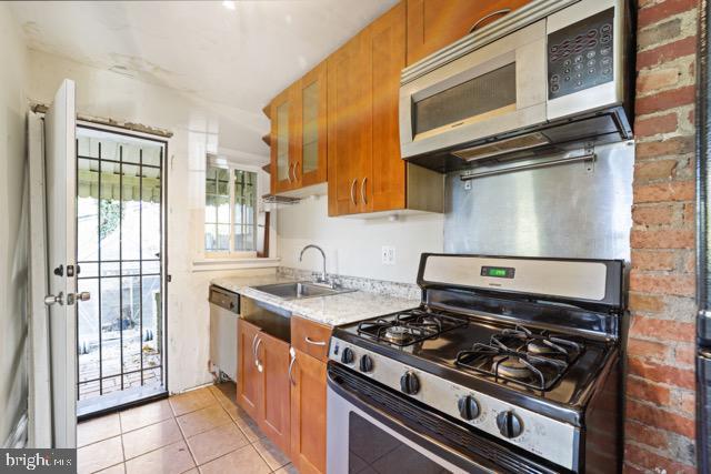 kitchen with appliances with stainless steel finishes, a sink, brown cabinetry, and light tile patterned flooring