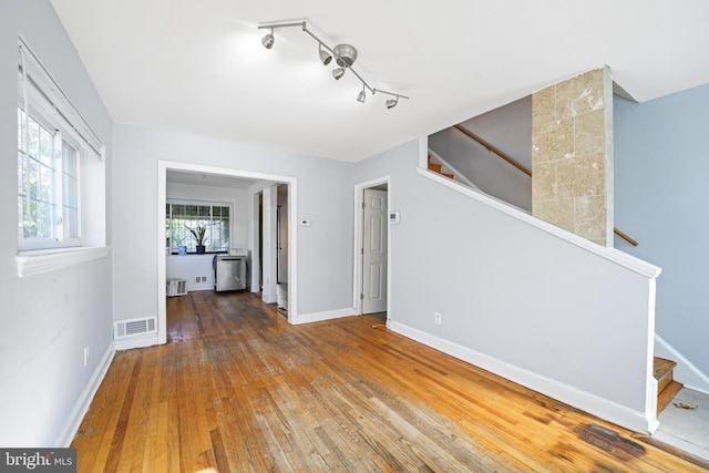 unfurnished living room featuring stairway, wood-type flooring, baseboards, and rail lighting