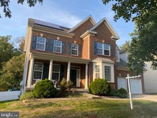 view of front of property with a front yard, solar panels, a garage, and a porch