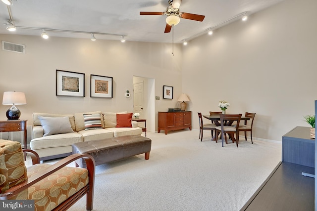 carpeted living room featuring ceiling fan, a high ceiling, and rail lighting