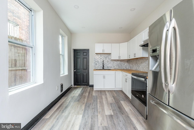 kitchen with white cabinetry, stainless steel appliances, wooden counters, extractor fan, and light hardwood / wood-style floors