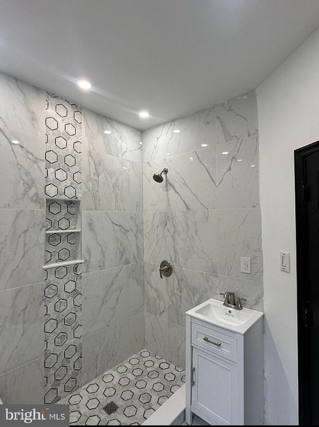 bathroom with tiled shower, vanity, and tile walls