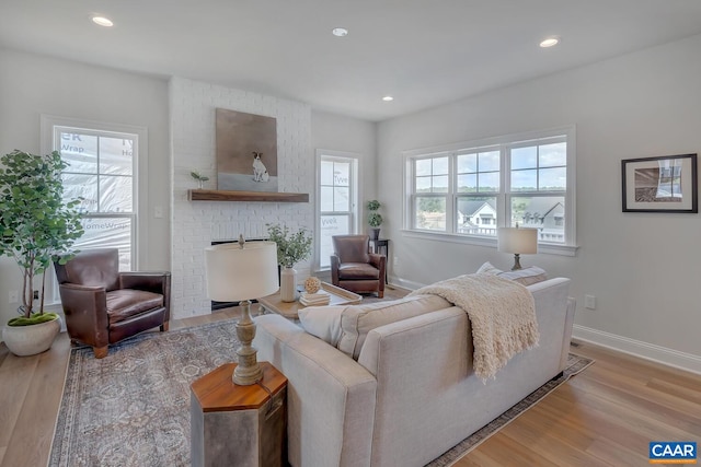 living room featuring a brick fireplace, light hardwood / wood-style floors, and a healthy amount of sunlight