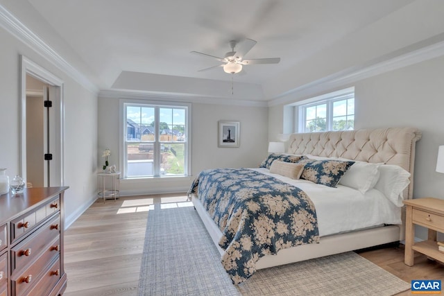 bedroom featuring ceiling fan, light wood-type flooring, multiple windows, and a tray ceiling